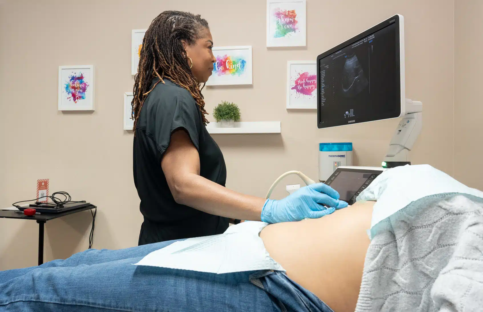 Sonographer performing abdominal exam with mobile diagnostic ultrasound equipment in an exam room